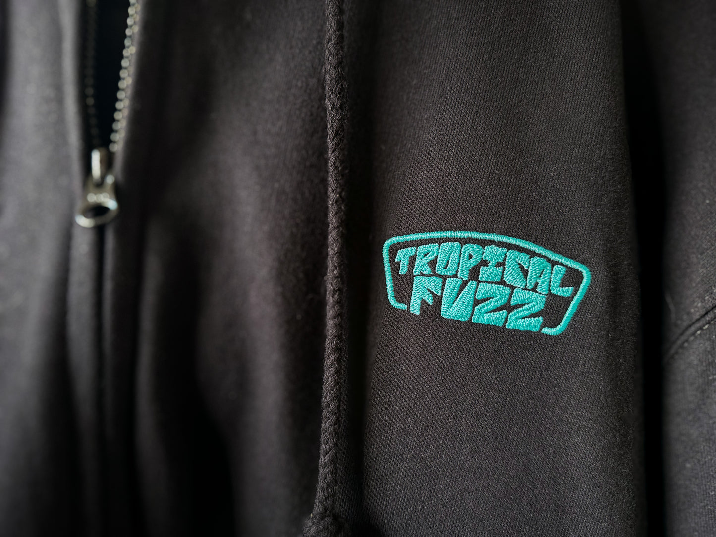Black zip hoodie with bright green embroidered 'Tropical Fuzz' logo