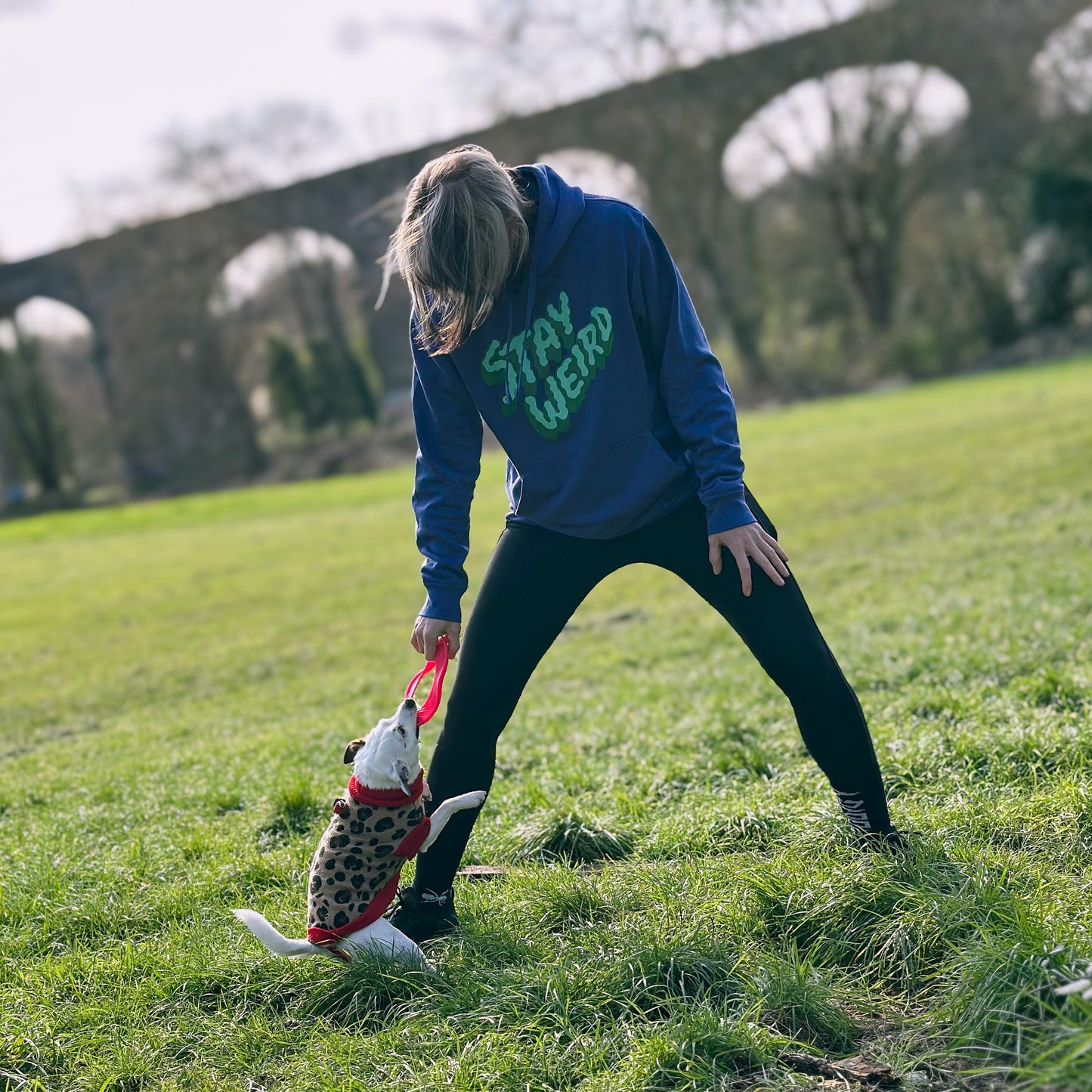 woman wearing a purple hoodie with the words 'stay weird' whilst playing with a dog