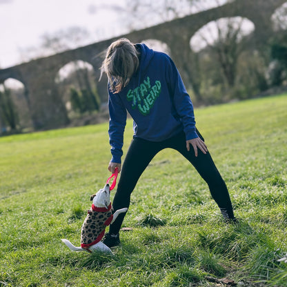woman wearing a purple hoodie with the words 'stay weird' whilst playing with a dog