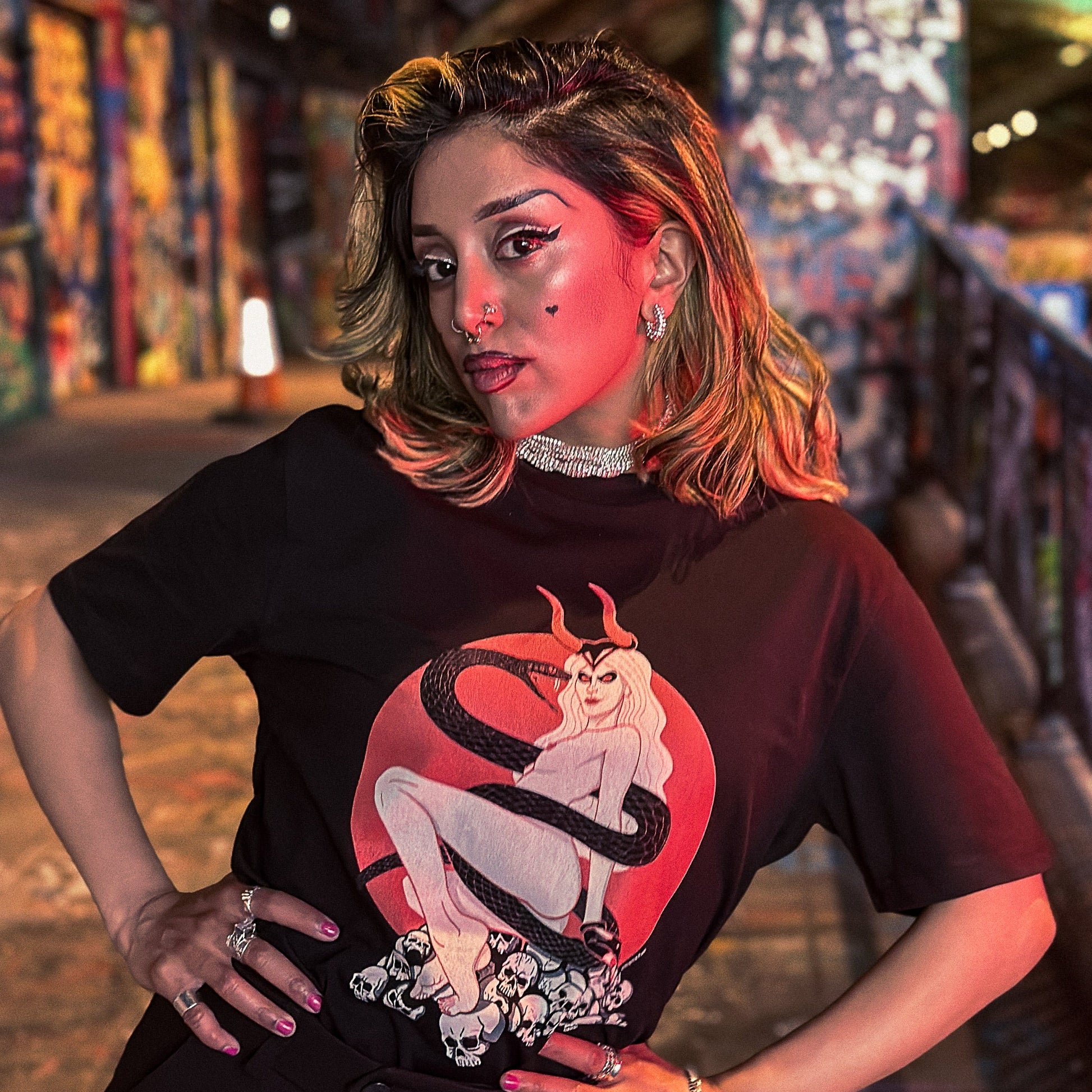 Person wearing a black t-shirt with a graphic design in a colorful, urban setting.