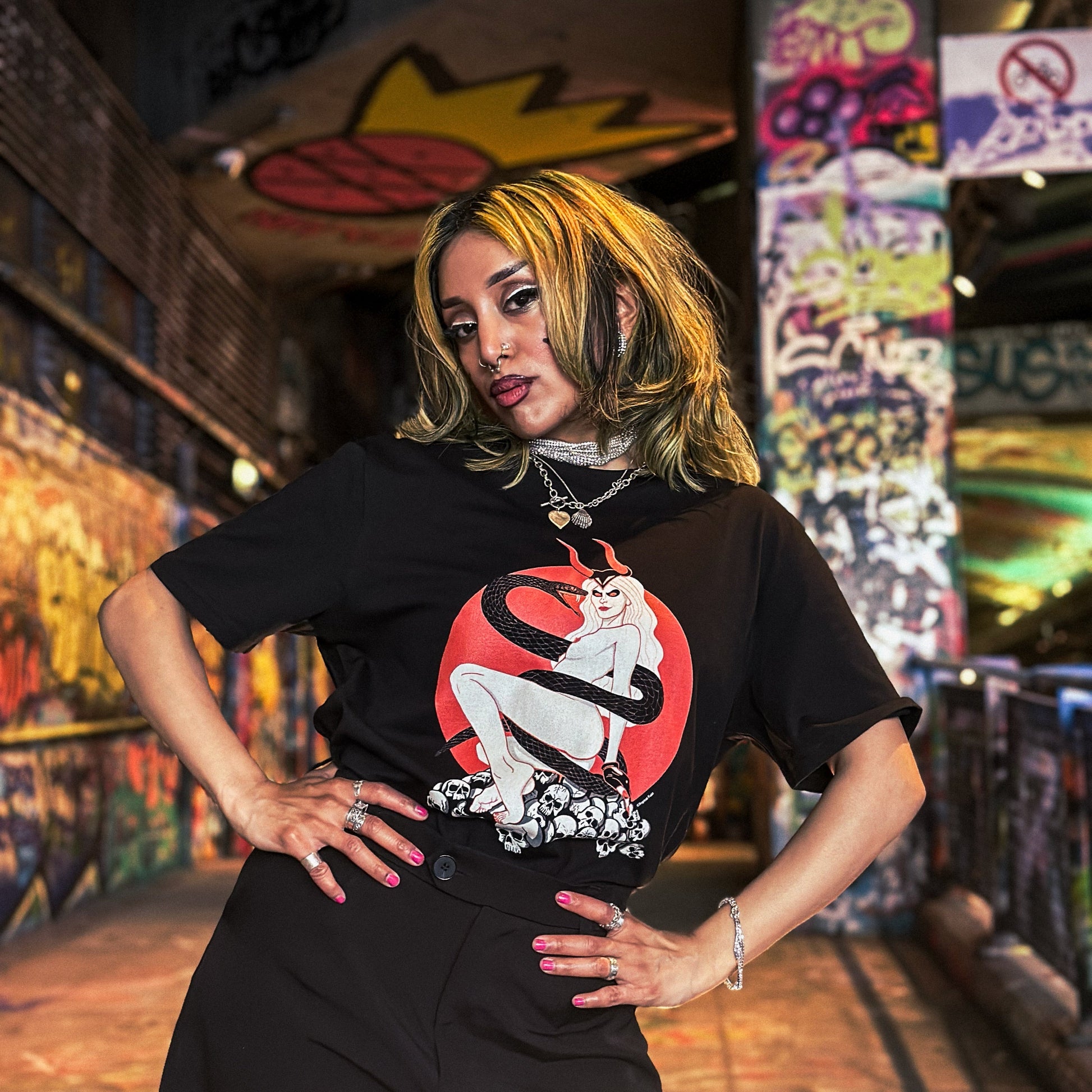 Person wearing a black t-shirt with a graphic design in a graffiti-covered alley.