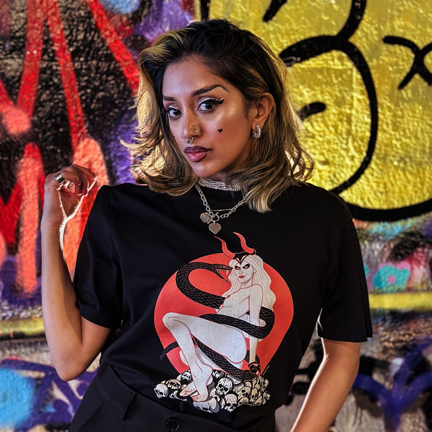 Person wearing a black t-shirt with a graphic design in front of a colorful graffiti wall.