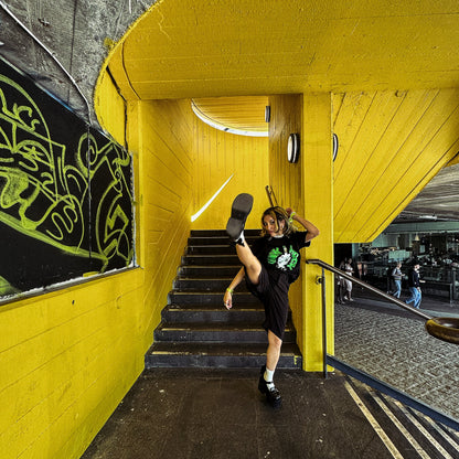 Person wearing black punk rock tshirt in an urban setting with yellow walls and stairs.