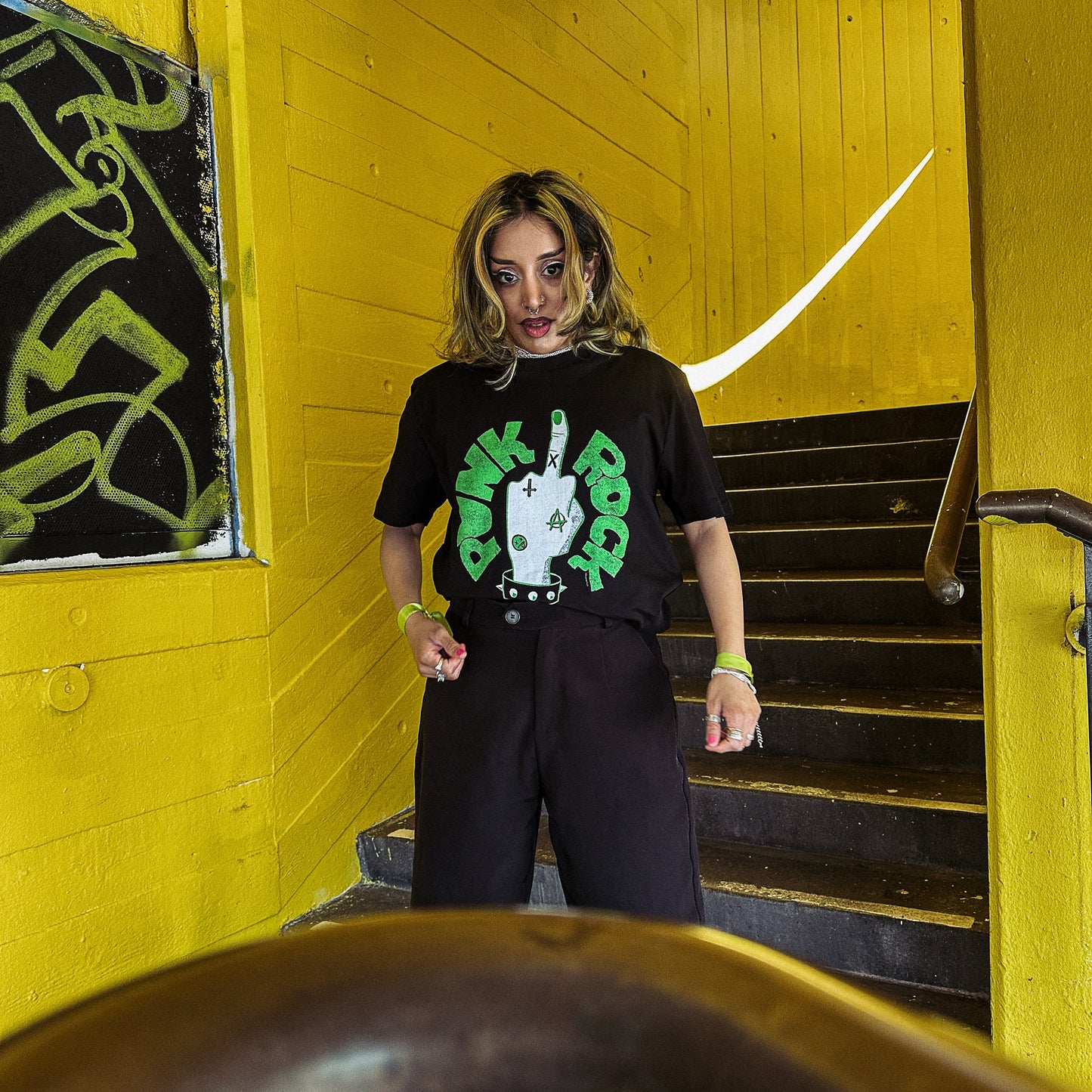 Person wearing a black t-shirt with a green graphic design in a yellow-walled room.