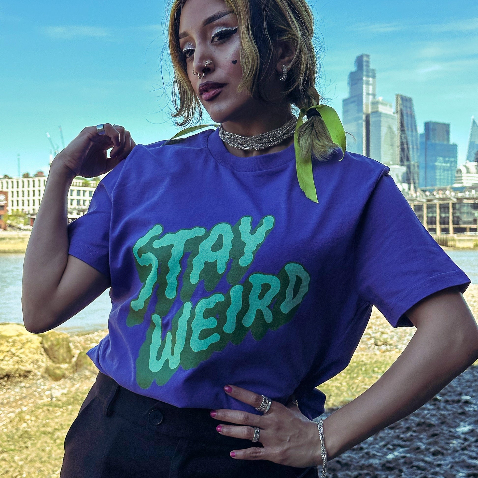 Person wearing a purple 'Stay Weird' t-shirt with a cityscape in the background