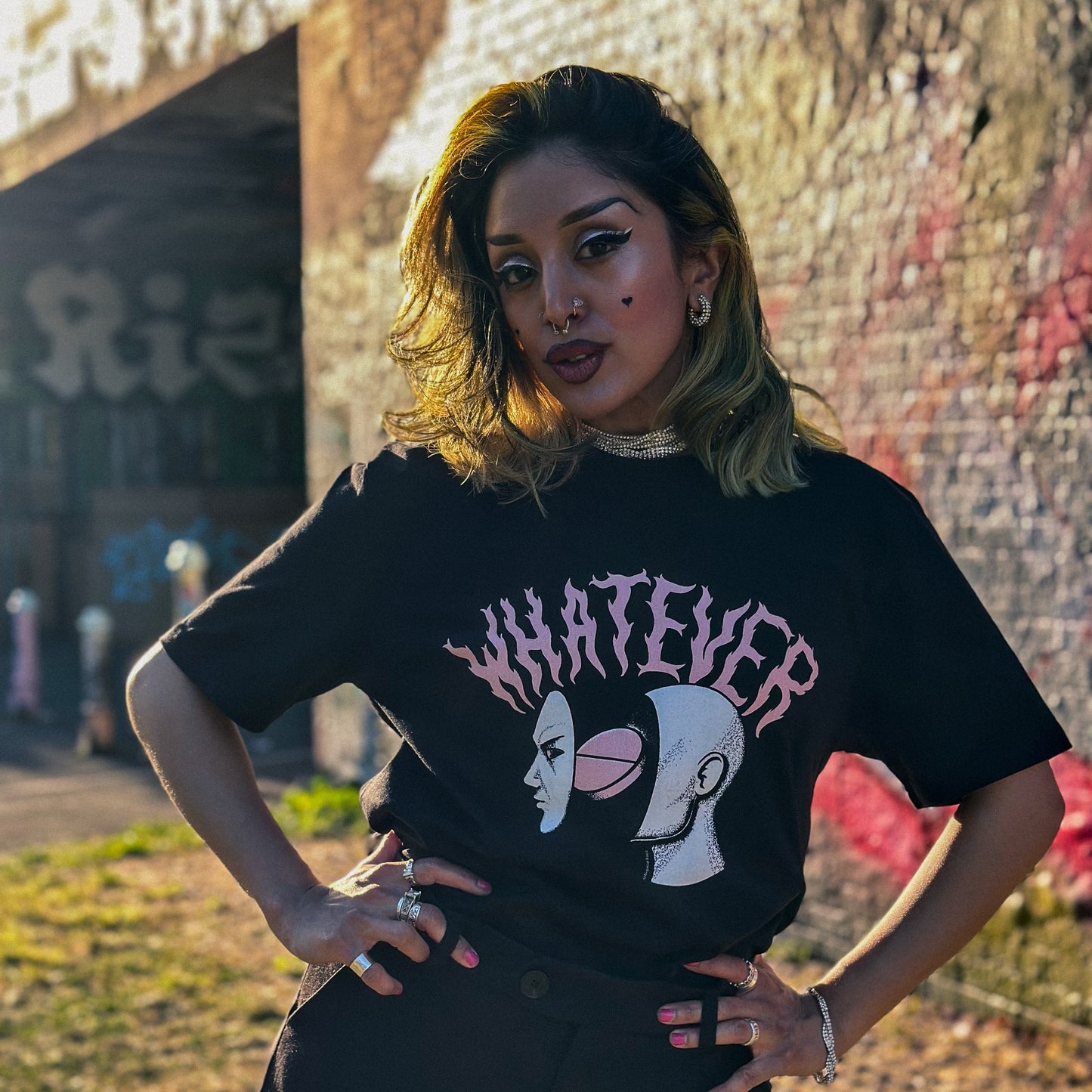 Person wearing a black t-shirt with a graphic design and text, standing in front of a graffiti-covered wall.