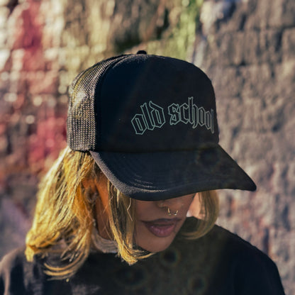 Person wearing a black cap with 'old school' text, against a textured wall background.