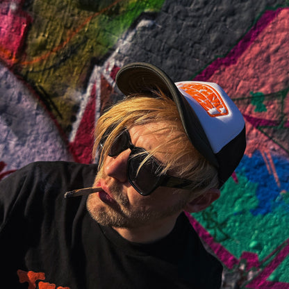 Person wearing sunglasses and a cap in front of a colorful abstract wall.